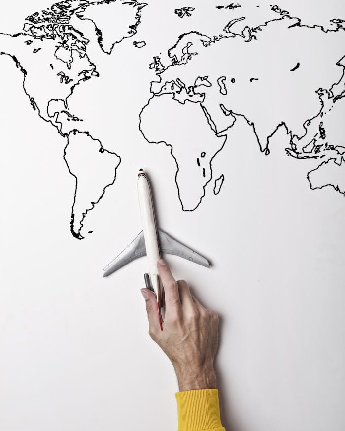 Crop person in vibrant yellow clothes holding little gray plane against contour map on white wall as concept of tourism and adventure