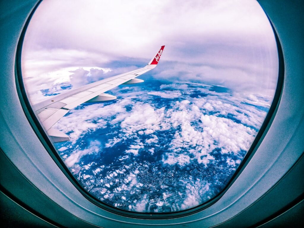 Wide angle of rocky ground through cloudy sky and plane wing from window of aircraft